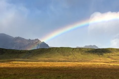 Rainbow in the clouds over the sunny hills in highlands of Iceland Stock Photos