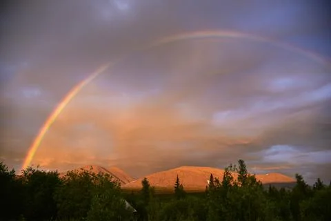 Rainbow in the cloudy sky at sunset. Scenic landscape - Mountains behind the Stock Photos