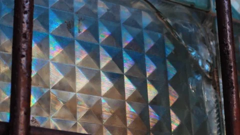 Rainbow coated broken window glass beneath a grill, reveal shot close up Stock Footage 107009103