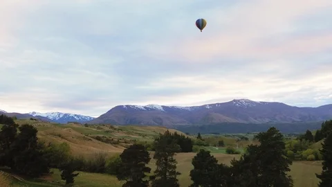 Rainbow colored hot air balloon high in sky above New Zealand countryside Stock Footage 90266934