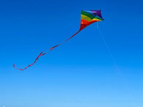 Rainbow Colored Kite Flies High Against Blue Sky Background Foto stock