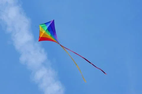 Rainbow colored kite flying below an aircraft vapor trail Stock Photos