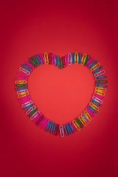Rainbow-colored paper clips layout as a big heart on red paper background, cr 库存照片