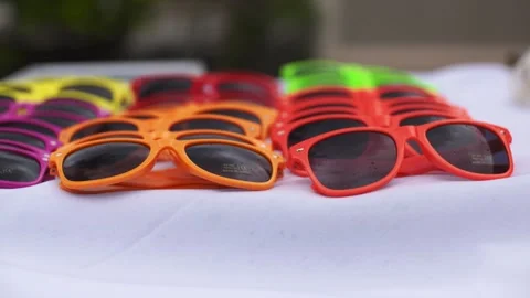 Rainbow colored sunglasses sit on white table during an outdoor party. Stock Footage 135236701