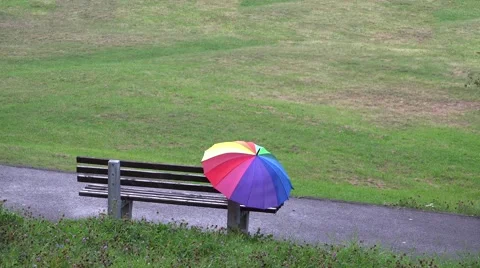 Rainbow colored umbrella abandoned on empty bench in the park, loneliness 4k Video stock 46213105