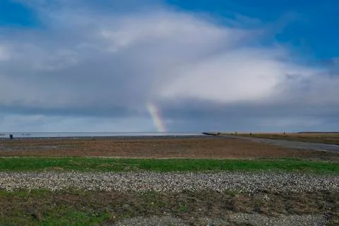 Rainbow with dark blue sky with clouds. grass and stones in foreground. Peopl Stock Photos