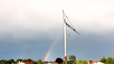 Rainbow disappearing on cloudy sky behind tall crane between roofs Time Lapse Stock Footage 156252352