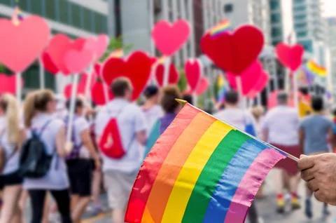 Rainbow flag floating in front of blurred gay pride participants Stock Photos