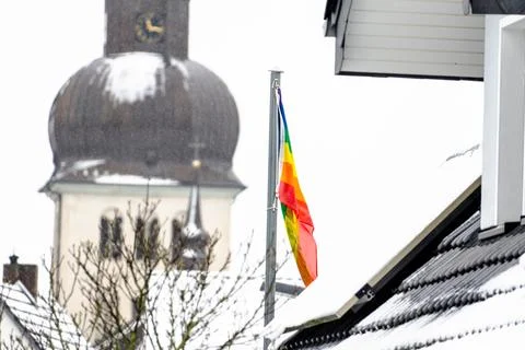 A rainbow flag is flying on a pole in front of a church Stock Photos