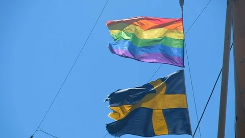 Rainbow flag on a ship coupled with the Swedish flag waving in slow motion Stock Footage 93668618