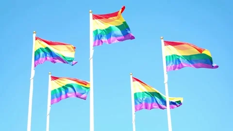 Rainbow flag waving in the wind against blue sky with clouds, sunny day, closeup Stock Footage 170003722