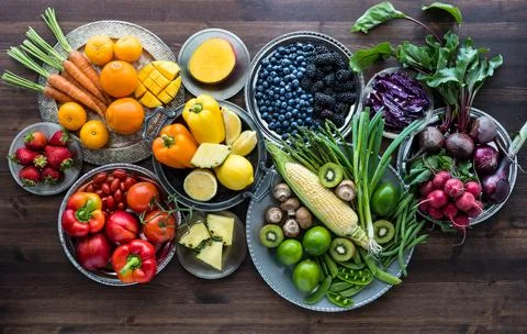 Rainbow fruit and vegetable flatlay arrangement against a dark wooden background Stock Photos