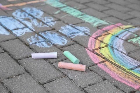 Rainbow with grass and clouds painted in colored chalk on a path on the stree Stock Photos