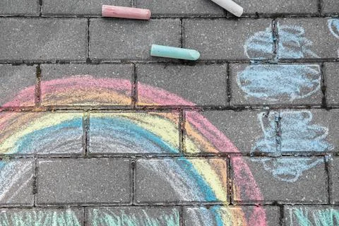 Rainbow with grass and clouds painted in colored chalk on a path on the stree Stock Photos