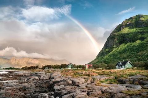 A rainbow juts out of the side of a mountain over the remote and colorful cab Stock Photos