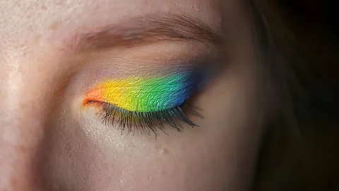Rainbow makeup on closeup blue eye of caucasian girl looking at camera and Video stock 99378260