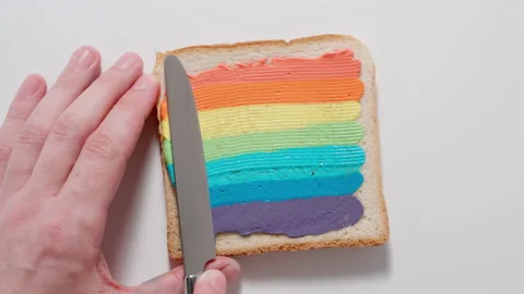 Rainbow. Male spreading colourful paste on a toast with knife. Top view. Stock Footage 144416742
