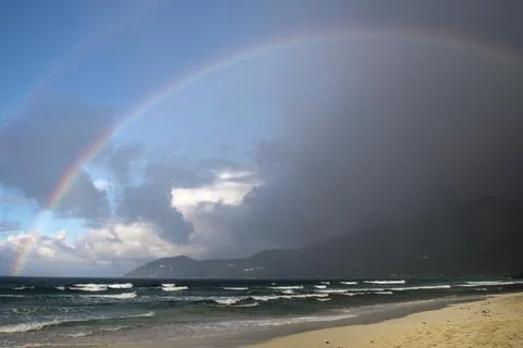 Rainbow over beach with black clouds and rain Фото