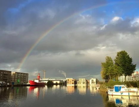 Rainbow over cloudy sky above harbour with light house boat Stock Photos