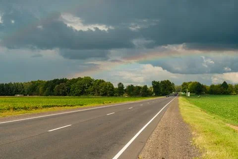 A rainbow over the road in the middle of green summer fields Stock Photos