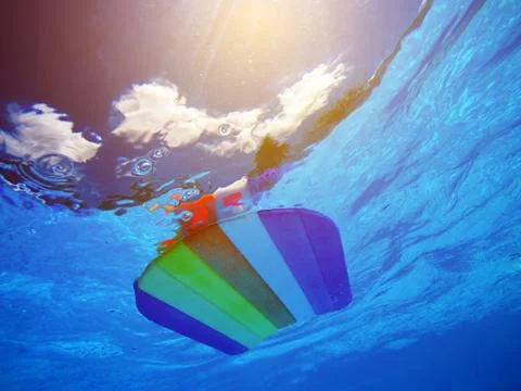 Rainbow pattern styrofoam swimming board floating in poolside water Foto stock