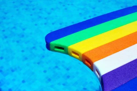 Rainbow pattern styrofoam swimming board baseboard floating in poolside water Foto stock