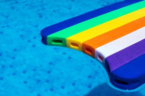 Rainbow pattern styrofoam swimming board baseboard floating in poolside water Stock Photos