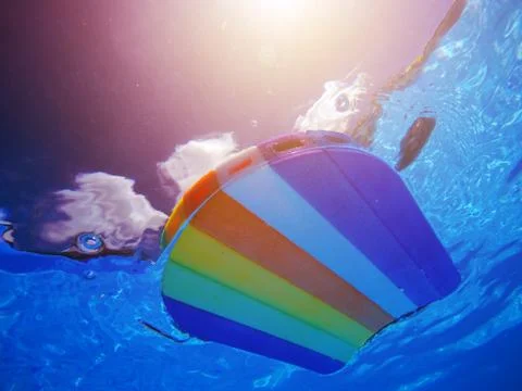 Rainbow pattern styrofoam swimming board floating in poolside water Foto stock