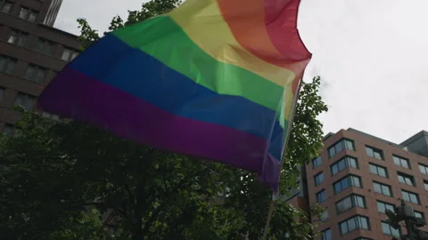 Rainbow pride flag flutters in the breeze against a backdrop of modern urban Stock Footage 346240340