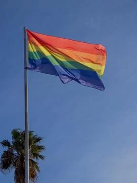 Rainbow Pride flag waving on flagpole against clear blue sky Stock Photos