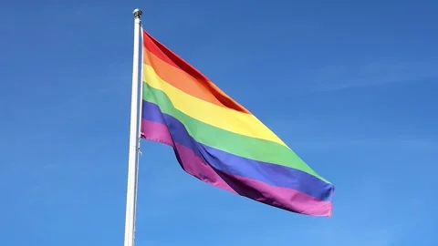 Rainbow pride flag waving in slow motion against a blue sky Stock Footage 345756699