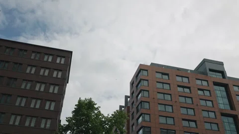 Rainbow pride flag waving in the wind against an overcast sky, two modern brick Stock Footage 346240322