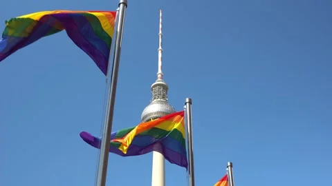 Rainbow pride flags high on pole in wind with Berlin TV tower in background Stock Footage 159665165