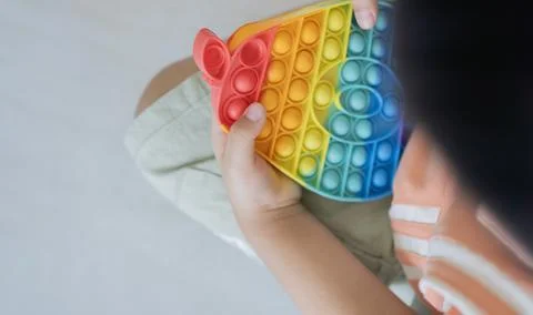 Rainbow push pop it bubble sensory fidget toy in hands of kid on its floor .. Stock Photos