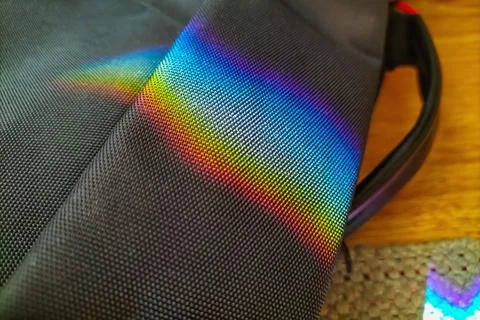 Rainbow reflection from mirror on black textured bag on floor. Interference Stock Photos