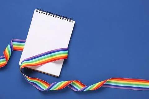 Rainbow ribbon with blank notebook on blue background. LGBT concept Stock Photos