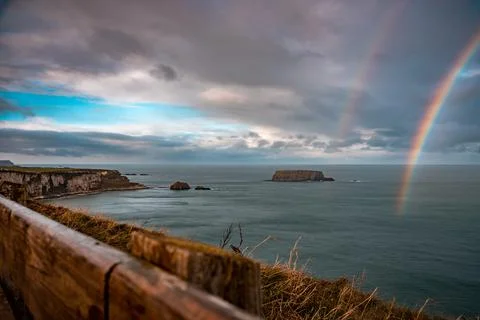 Rainbow shining between rainy clouds, sea and cliffs near Ballintoy in Northern Stockfoto's