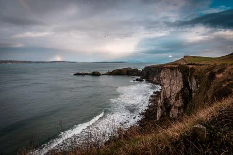 Rainbow shining between rainy clouds, sea and cliffs near Ballintoy in Northern Stock Photos