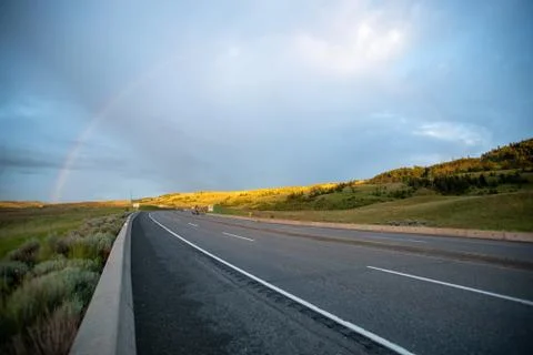 A rainbow shining beyond an empty countryside highway. Stock Photos