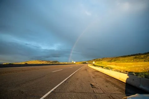 A rainbow shining beyond an empty countryside highway. Stock Photos