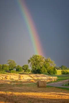 Rainbow shining over a post-rain harvest landscape at dusk. Stock Photos