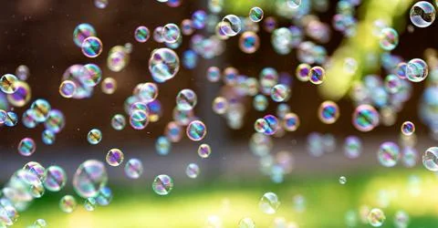 Rainbow soap bubbles floating outdoors. Bright summer background with green.. Stock Photos