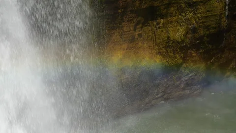 Rainbow in the spray at the bottom of a rocky waterfall Video stock 135473225