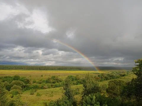 Rainbow in summer over the river, forest and fields, clouds with blue gaps .. Stock Photos