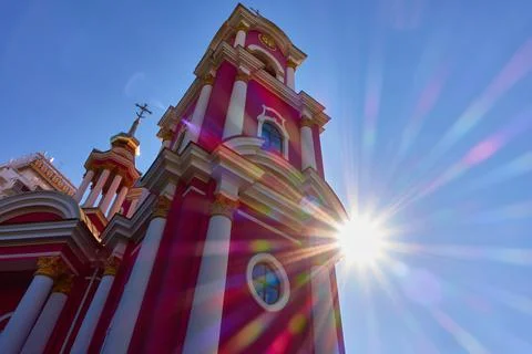 A rainbow sun peeks out from behind a church with golden domes and red walls Stock Photos
