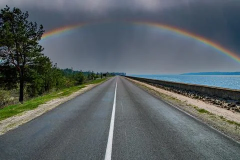 A rainbow with a thundercloud on the horizon of a highway. 스톡 사진