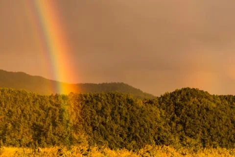 Rainbow touching of colors on a cloudy day breaking through the clouds and to Stock Photos