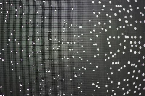 Raindrops and bokeh lights on window screen mesh at night Stock Photos