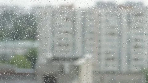 Raindrops are running down the glass, outside the window there is a blurred urba Video stock 205460440