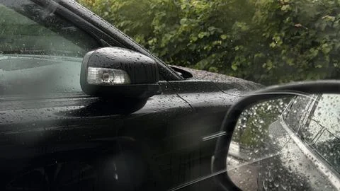 Raindrops on a black vehicle's side mirror and window. Close-up view of a wet Stock Photos